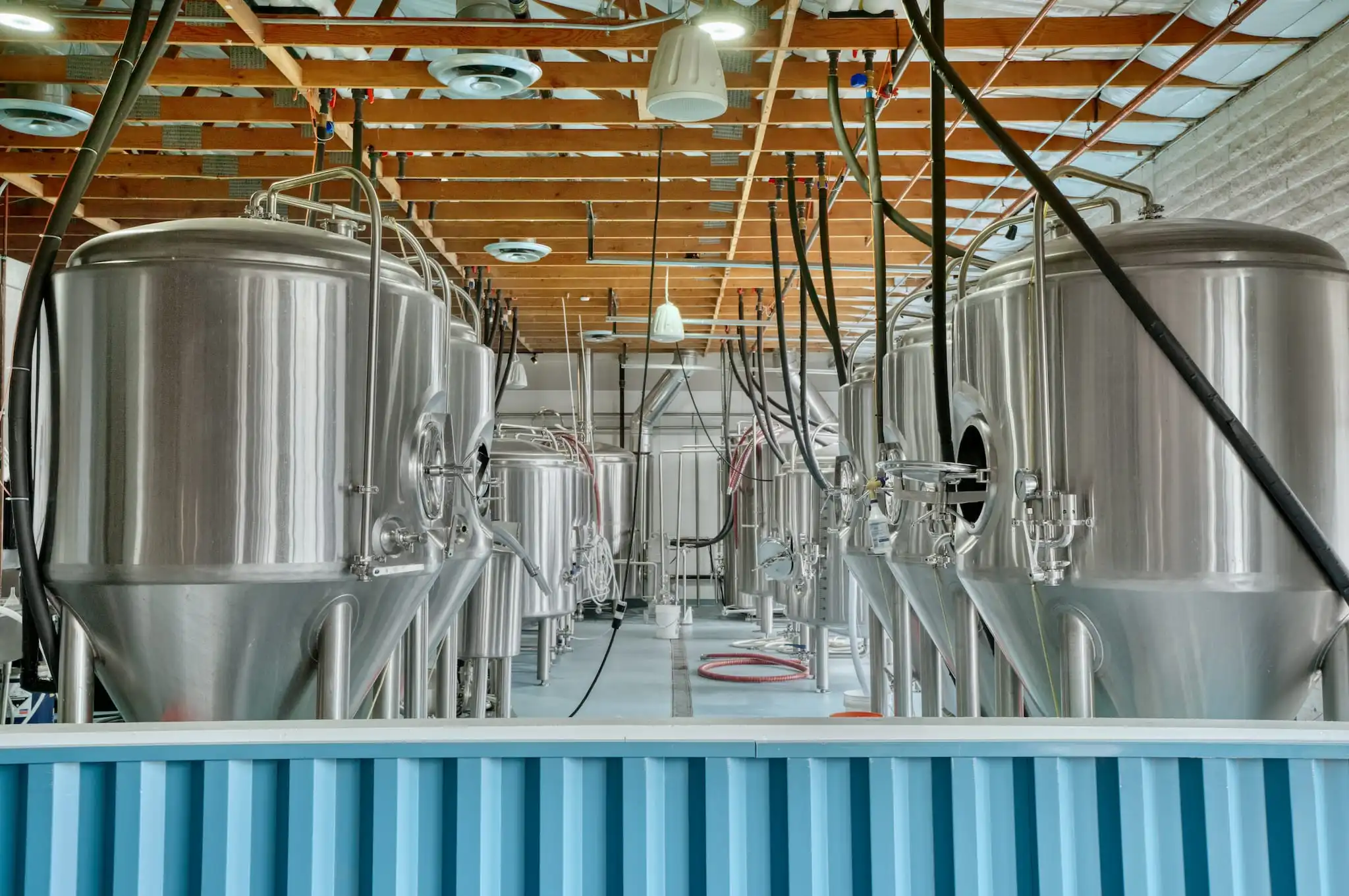 Stainless fermenters in the Hundred Mile brewhouse, behind a blue corrugated wall.