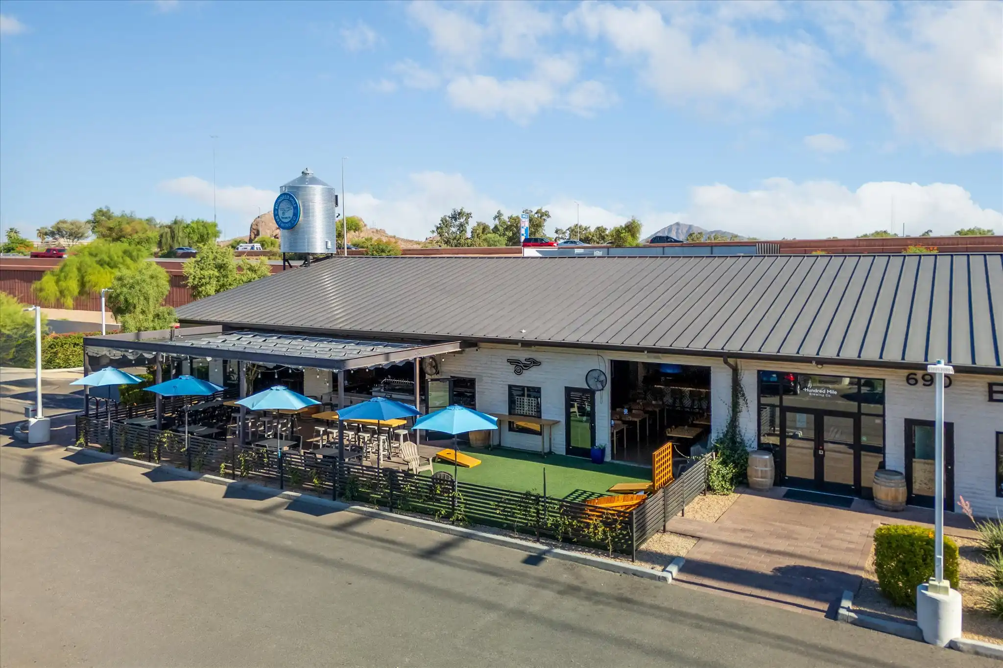 Daytime patio with picnic tables and blue umbrellas in front of the brewery.